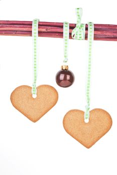 Homemade gingerbread hearts and christmas ball hanging from branches isolated over white background. Traditional christmas concept.