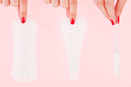 Female hand with red fingernails holding a clean pantyliner, g - string pantyliner and a tampon isolated over pink background. Feminine hygiene concept.