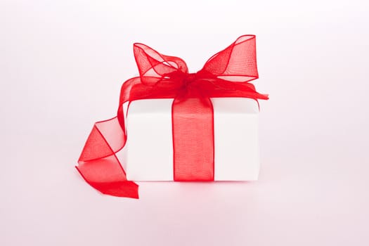 Luxurious white present with red ribbon on pink background. Festive giving concept.