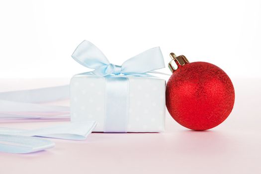 Luxurious gift and christmas ball with ribbon on light pink background. Festive holiday background, giving concept.