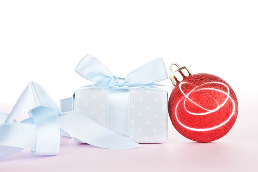 Luxurious gift and christmas ball with ribbon on light pink background. Festive holiday background, giving concept.