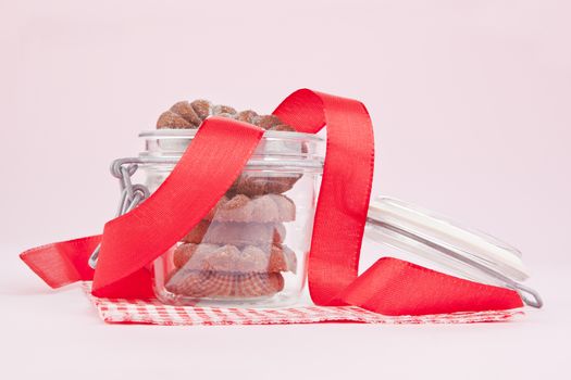 Chocolate cookies in glass jar with red ribbon on pink background. Mouthwatering yummy concept.