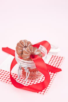 Chocolate christmas cookies with red ribbon in glass jar on napkin on pink background. Christmas concept. 