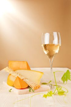 Luxurious wine background. White wine in wine glass and cheese variation on wooden background.