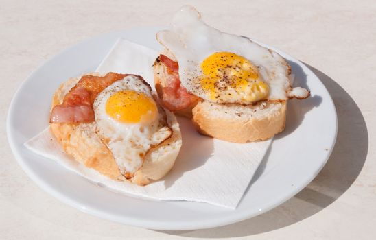 Dish with quail eggs and bacon sandwich outdoors.