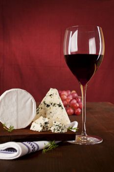 Traditional dark red wine background with blue  cheese and grapes on dark wooden background.