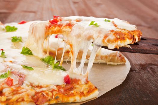 Delicious hot pizza piece on wooden spoon with melting cheese. Rustic pizza concept.