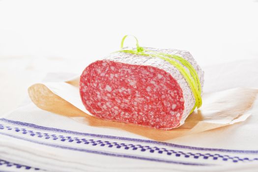 Luxurious salami piece cut on baking paper on kitchen cloth. Culinary meat background.