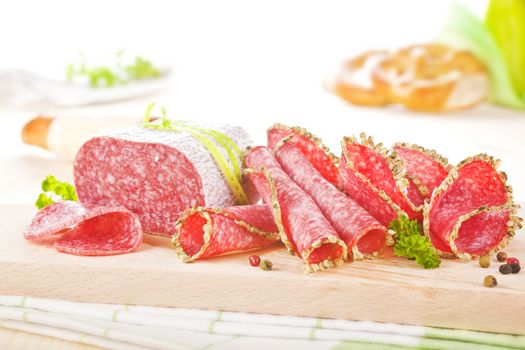 Luxurious salami slices arranged on wooden board with fresh herbs and pepper corns. Culinary eating.