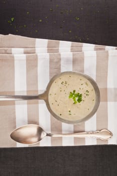 Mushroom cream soup in silver soup scoop with antique silver spoon on kitchen cloth. Luxury eating.