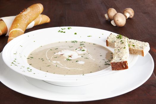 Champignon mushroom cream soup in white plate with pastry on dark wooden background. Culinary eating.