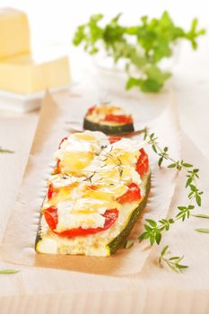 Baked zucchini slices with fresh tomatoes, cheese and herbs. Cheese and fresh herbs in background. Culinary healthy food.