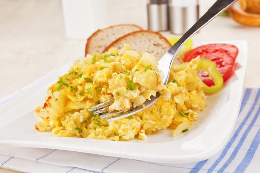 Scrambled eggs on fork, pastry, salt and pepper shaker in background. Culinary breakfast concept.