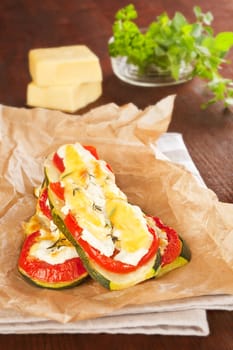 Baked zucchini with tomato and cheese on baking paper on wooden background. Culinary eating.