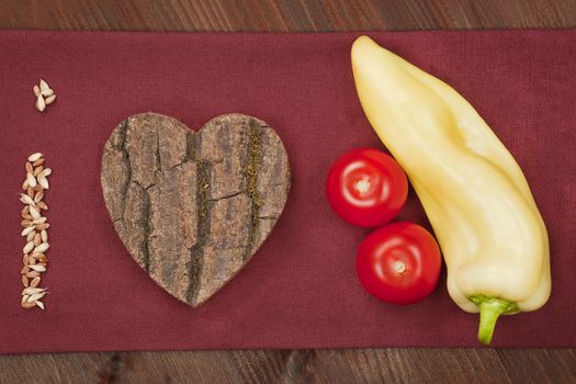 I love vegetable made of seeds, wooden heart, tomatoes and green pepper on burgundy cloth. Agriculture background.