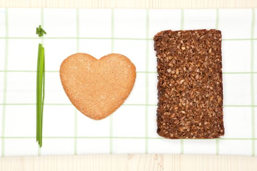 Heart shaped biscuit, fresh chive and black bread slice making "I love healthy food" text background.