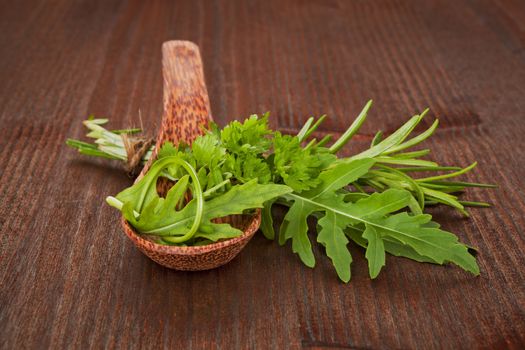 Fresh organic herbs on wooden spoon and wooden table. Aromatic culinary herbs mix. Parsley, roquette and rosemary.