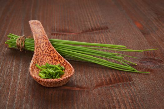 Fresh organic chopped chive on wooden spoon and chive bunch on dark wooden background. Aromatic culinary herbs.