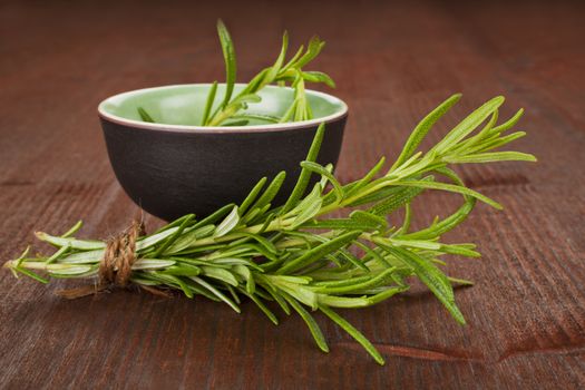 Rosemary bunch bound with natural twine on dark wooden background and in round cup. Aromatic culinary herbs.
