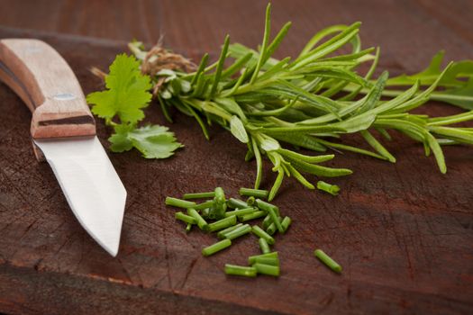 Various culinary organic herbs on dark wooden background with knife. Rosemary, coriander and chive.