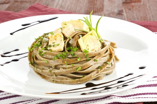 Culinary eating. Delicious homemade tagliatelle with artichoke on white plate with garnish on wooden table.