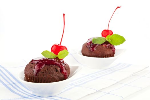 Two delicious homemade chocolate muffins decorated with jam, cherry and fresh mint leaf on kitchen cloth.