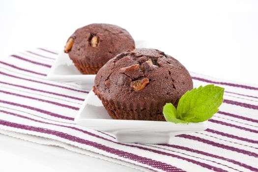 Delicious chocolate muffins with fresh mint on luxurious kitchen cloth.