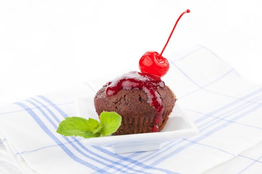 Delicious chocolate muffin decorated with cherry, jam and fresh mint leaf.