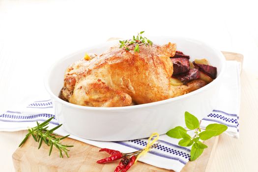 Golden grilled chicken with fresh herbs and vegetables in baking dish prepared for eating.