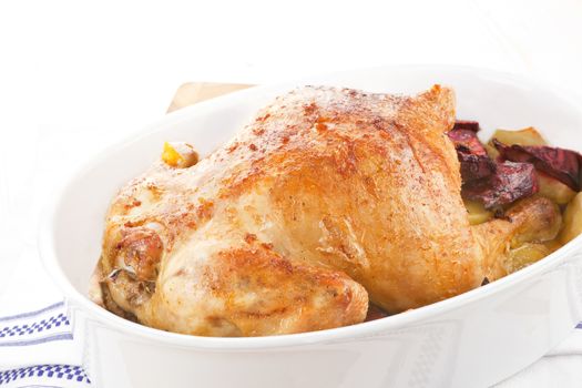 Luxurious golden whole chicken with potatoes and beet in baking dish.