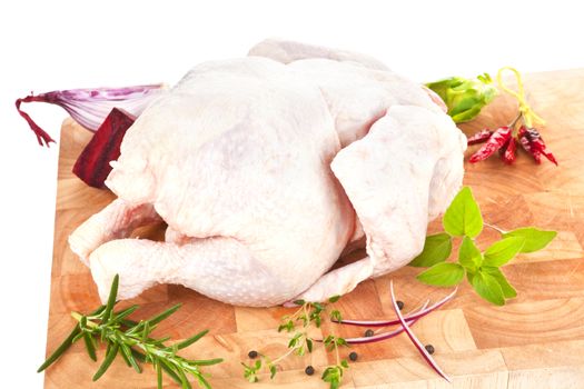 Whole raw chicken on wooden board with fresh herbs, spices and vegetable. Poultry background.