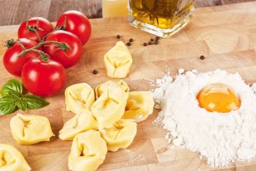 Tortellini pasta, tomatoes, flour with yolk and olive oil on wooden kitchen board.