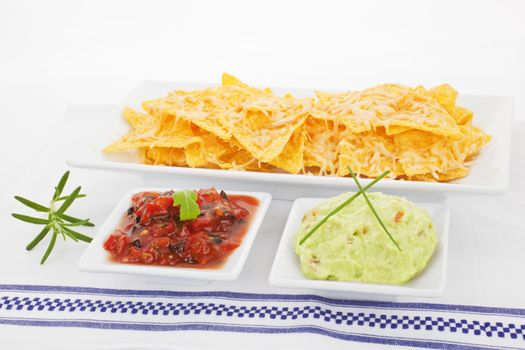 Nachos baked with cheese, guacamole and tomato dip in bowls decorated with fresh herbs.