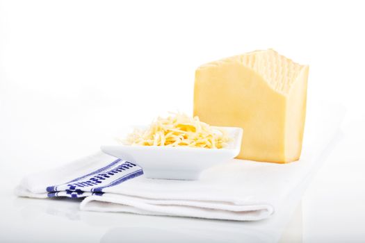 Grated cheese in white bowl and big gouda piece isolated on white.