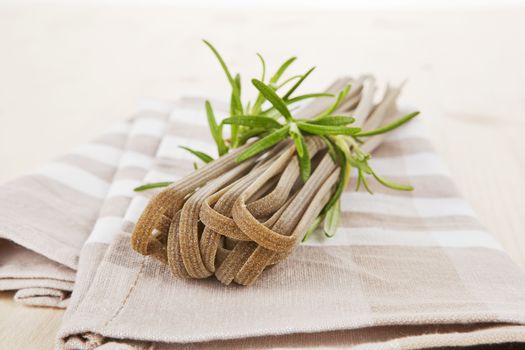 Whole grain tagliatelle with fresh rosemary on kitchen towel.