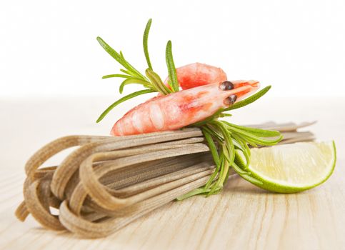 Whole grain pasta with shrimp, fresh rosemary and lime piece on wooden table.