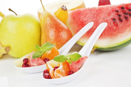 Delicious fruits pieces on white spoon. Healthy summer fruit background. Eat right, exercise regularly, die anyway. 