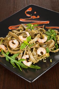Delicious tagliatelle with shrimps and fresh arugula on black plate with garnish