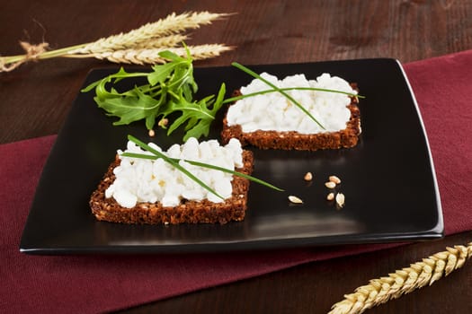 Black bread slices on black plate with cottage cheese and fresh herbs. Healthy eating background.