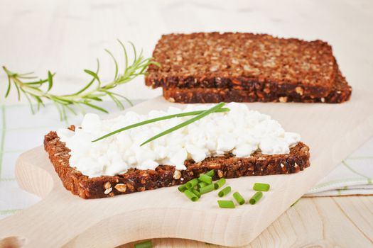 Delicious healthy breakfast. Black bread with cottage cheese and fresh herbs on wooden cutting board.