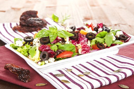 Delicious vegetable mix salad on white plate with dried tomatoes and seeds.