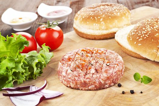 Cooking hamburger. Minced raw meet with fresh vegetable and bun on wooden cutting board. 