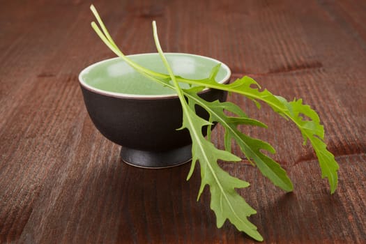 Fresh arugula leaves in black cup on dark wooden background. Culinary herbs concept.