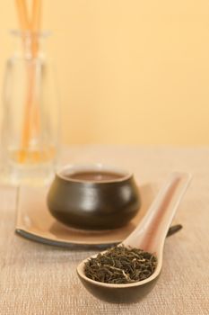 Black tea leaves on spoon, tea in tea bowl in background.
