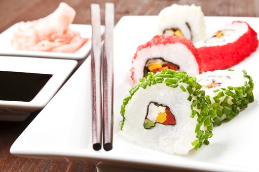 California sushi rolls with chive and caviar on white plate with chopsticks, soy sauce and ginger.