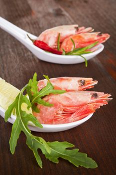 Luxurious seafood. Shrimps on white spoon with herbs close up.