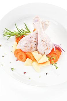 Raw chicken legs with fresh vegetables and spices on white plate isolated.