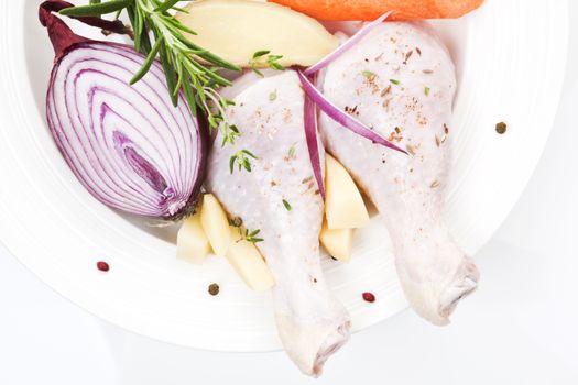 Raw chicken thighs with fresh vegetables onion, rosemary on white plate close up.