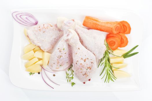 Raw chicken legs with potatoes, onions and carrots on white tray isolated on white background. 