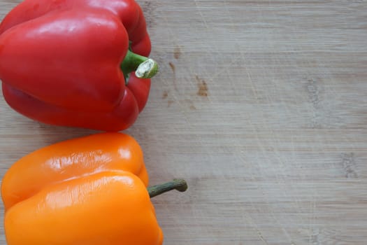 A red and orange pepper on a wooden cutting board